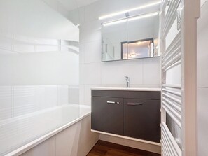 A modern bathroom with a white bathtub, a dark vanity with a mirror, and a light fixture above the mirror. - Economic Apartment, 4 Rooms, Ski-In/Ski-Out, 6 Pers, Wifi, Parking (Les Menuires)