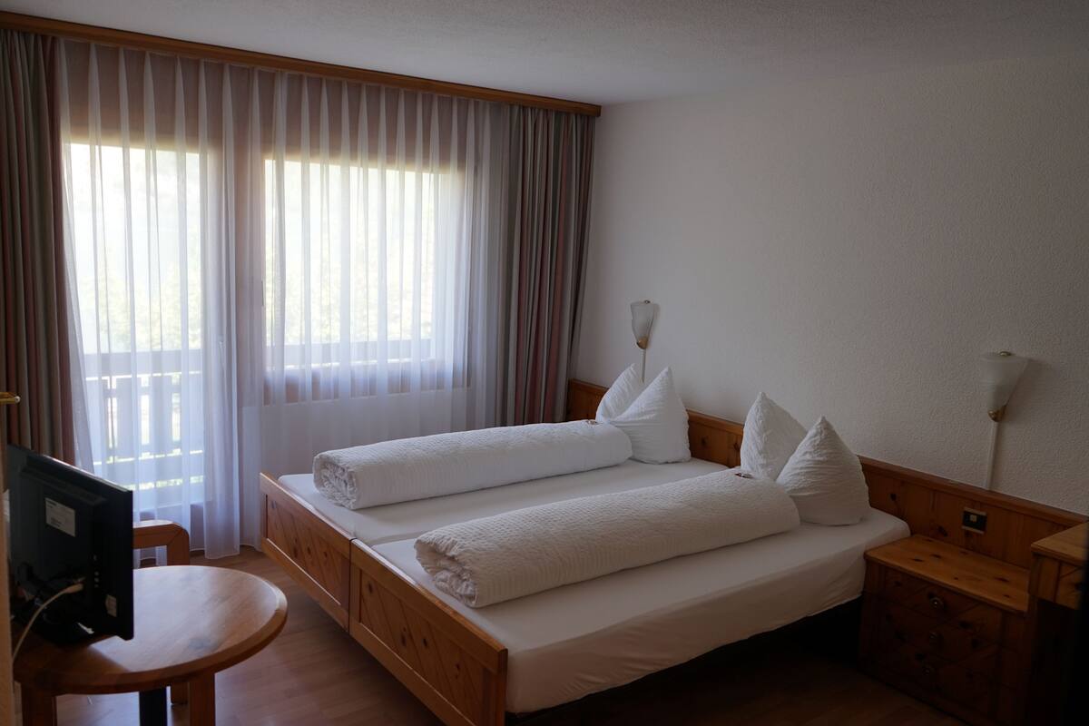 Habitación de hotel con dos camas, un escritorio de madera, una silla y un televisor.