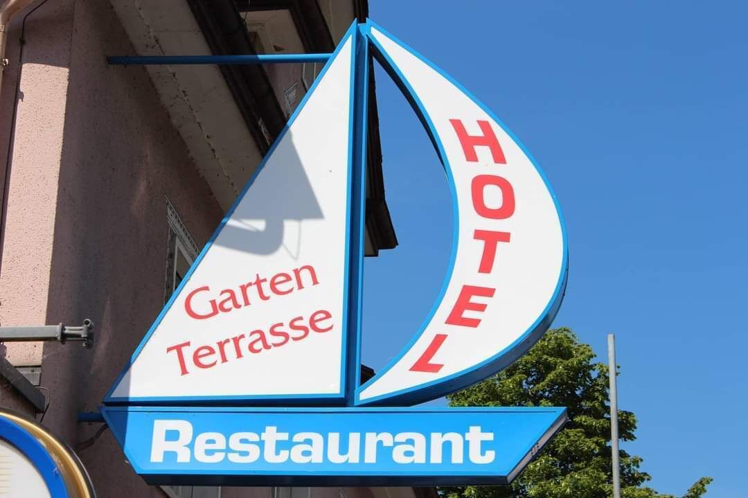 Une enseigne d'hôtel portant le nom « Garten Terrasse » et le mot « HÔTEL » sur un fond bleu.