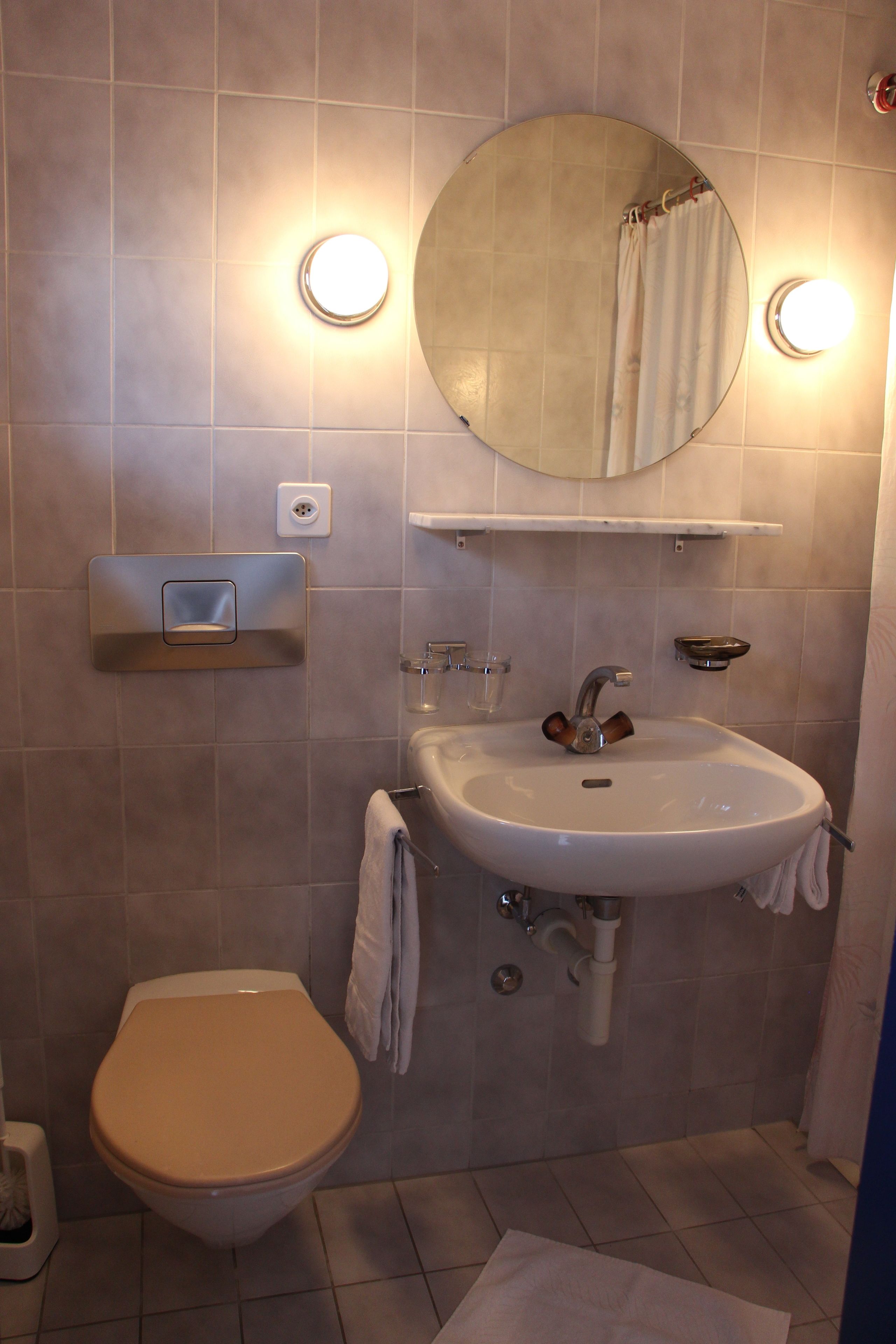 Un baño con inodoro, lavamanos, espejo y toallero.