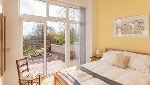 Une chambre dotée d’un grand lit, d’une chaise, d’une table de chevet et offrant une vue sur un jardin grâce à une porte-fenêtre coulissante.