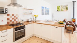 Une cuisine moderne avec des armoires blanches, un comptoir en bois, un four encastré et une cuisinière. On y trouve également un coin repas avec un fauteuil en cuir marron et une petite table.