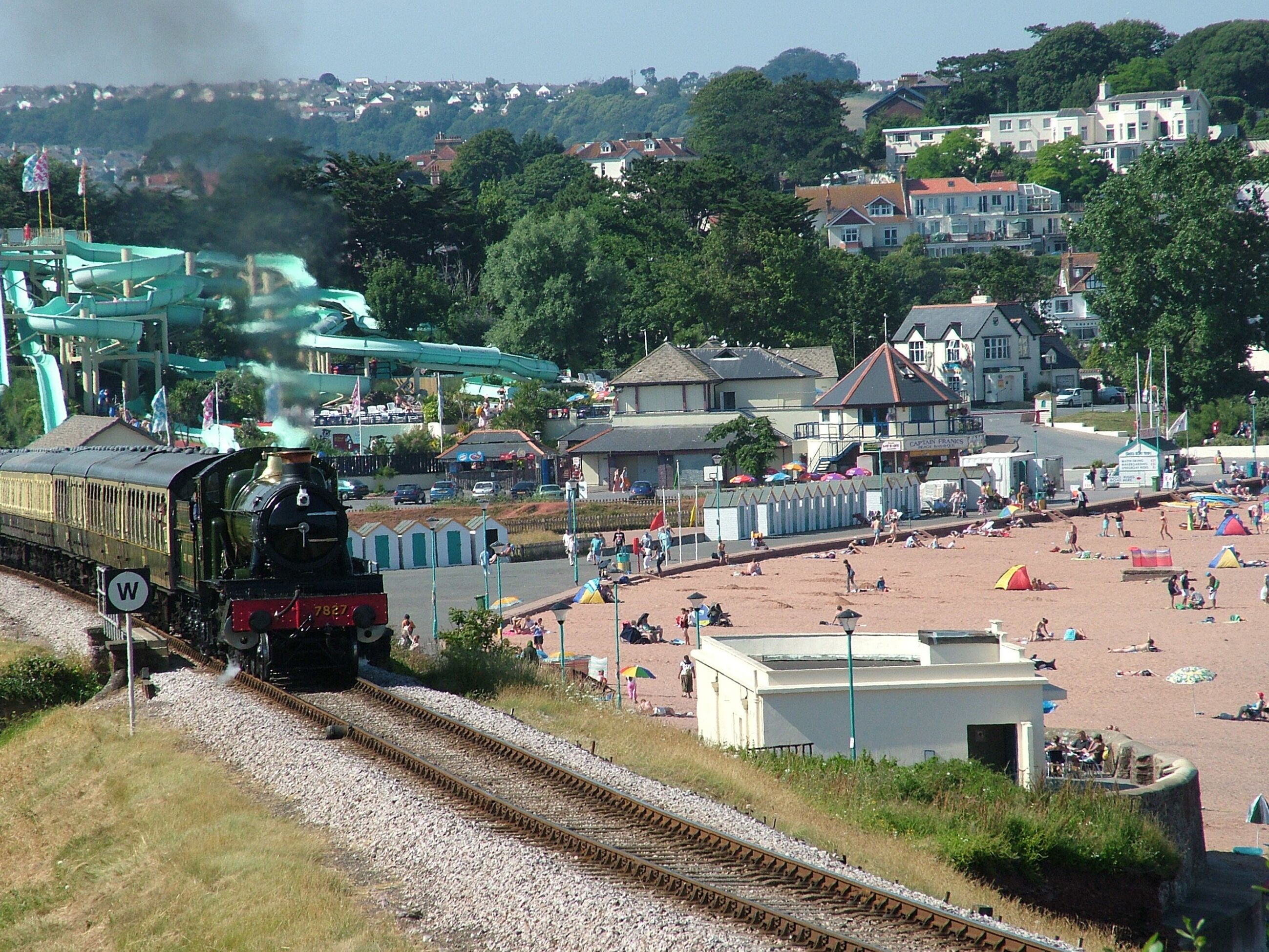 Un train circulant sur des voies ferrées, avec un parc aquatique et une plage en arrière-plan.
