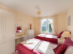 A bedroom with two beds, a desk, a dresser, a mirror, and a window with curtains.