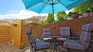 Een terras met een blauwe parasol, streepstoelen en een bakstenen muur.