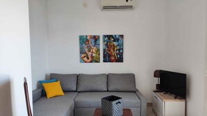 A living room with a grey sofa, a wooden coffee table, a television, and two abstract paintings on the wall. - Holiday apartment with a view of the lake (Primošten)