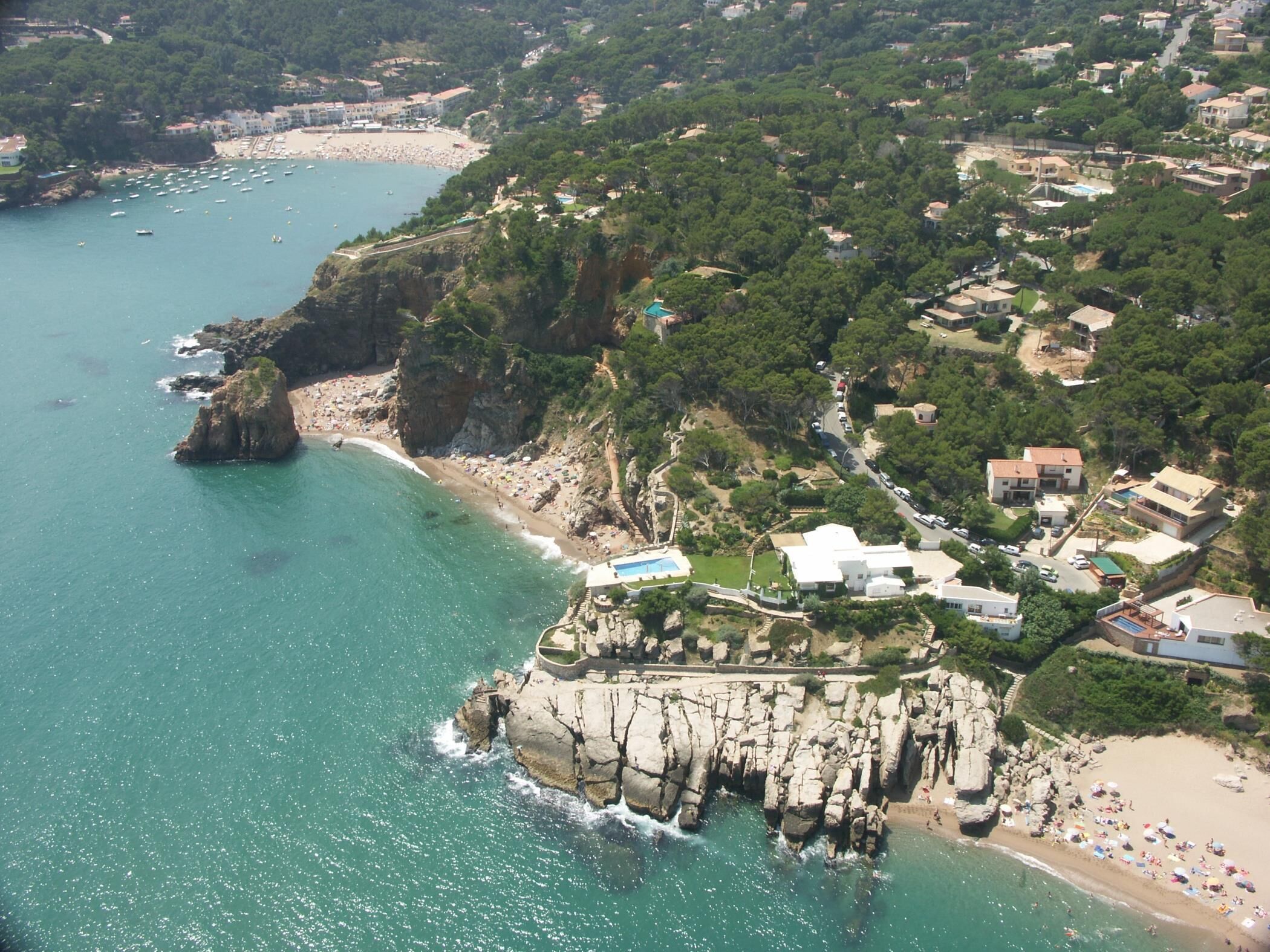 An aerial view of a coastal town with a rocky beach, clear blue waters, and residential buildings.