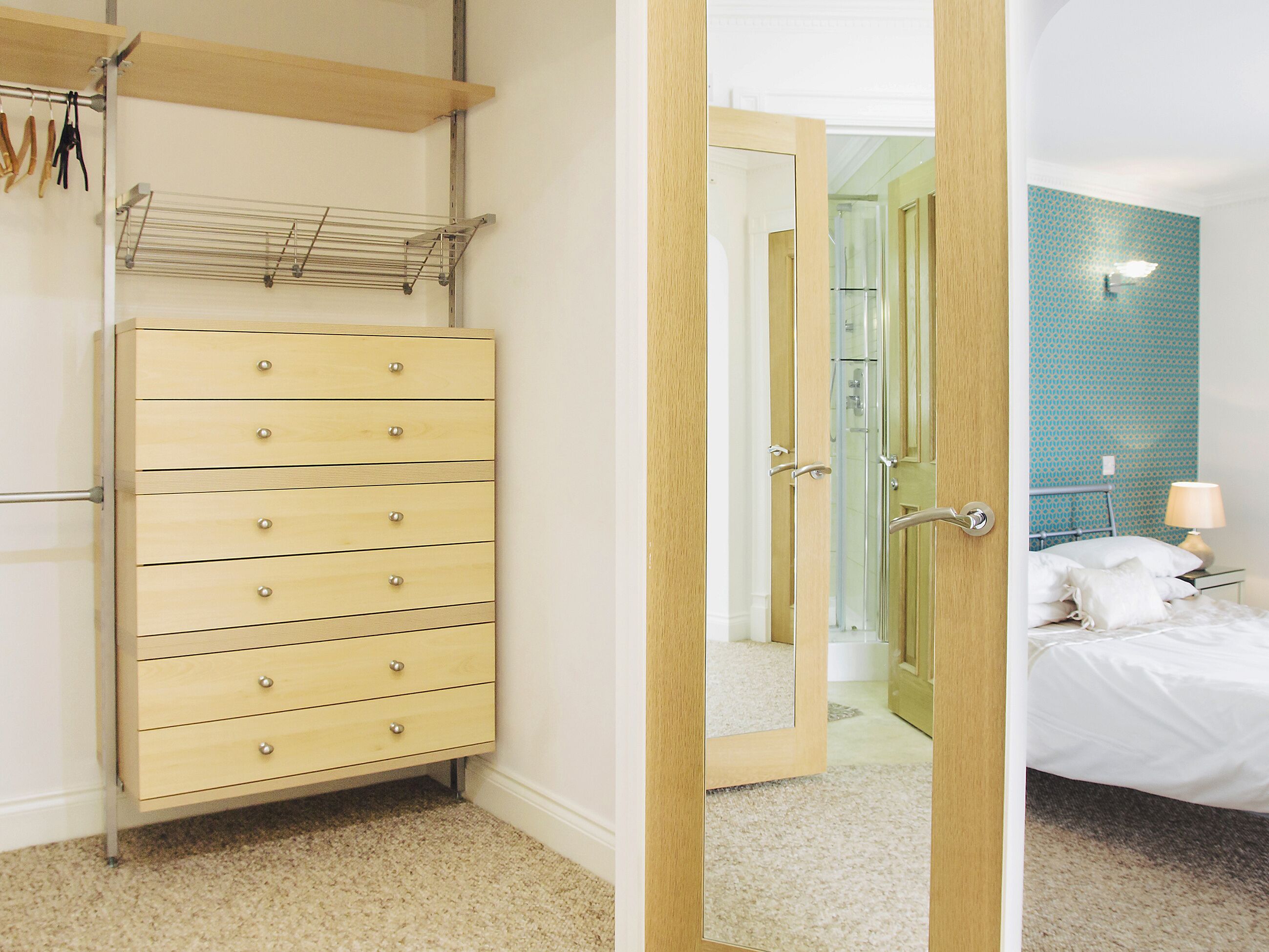 Une chambre d’hôtel avec une commode en bois, un miroir, un lit et une salle de bain visible à travers une porte ouverte.