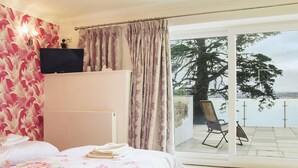 A bedroom with a bed, a window with curtains, a chair outside, and a view of the sea. - 2 bedroom accommodation in Torquay (Torquay)