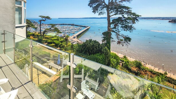 A balcony with a glass railing overlooking a marina, a beach, and a clear blue sky. - 2 bedroom accommodation in Torquay (Torquay)