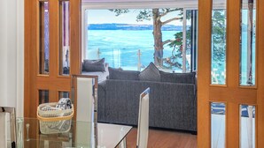 A room with a glass table, a grey sofa, and a view of the sea through large windows. - 2 bedroom accommodation in Torquay (Torquay)