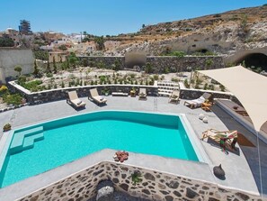 A swimming pool with lounge chairs, surrounded by stone walls and plants, with a view of a hillside town in the background.