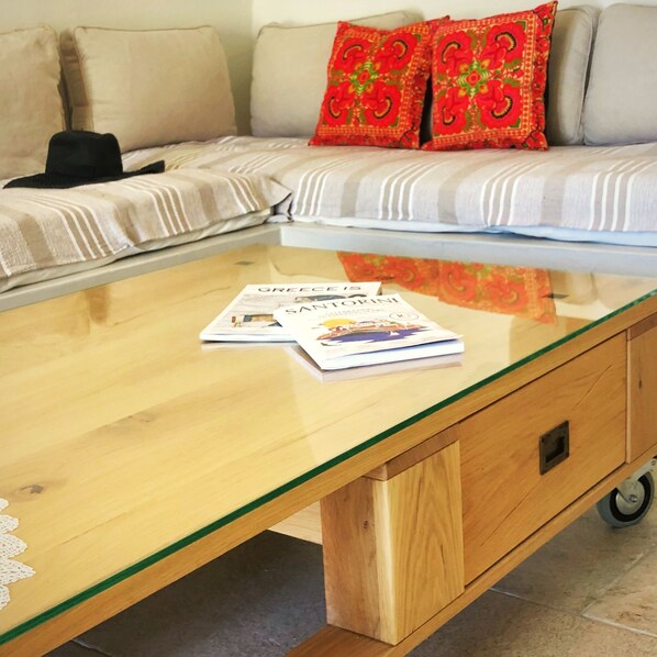 A room with a glass-top coffee table, a sofa with striped cushions, and a pair of red floral pillows.