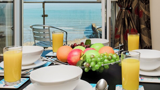 Une table de petit-déjeuner avec des fruits, des verres de jus d’orange et une vue sur la mer.