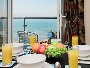 A breakfast table with fruit, glasses of orange juice, and a view of the sea.