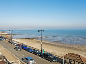 Eine Küstenstraße mit parkenden Autos, einem Strand und wolkenlosem Himmel.