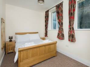 A bedroom with a wooden bed, white linens, a nightstand with a lamp, and floral curtains.