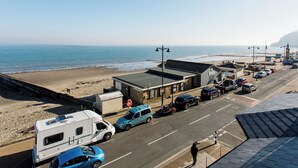 Une route côtière bordée de véhicules garés, une plage et un bâtiment avec une enseigne.