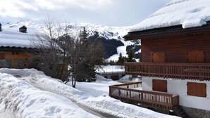 Eine Holzhütte mit Balkon, umgeben von schneebedeckten Bergen und einem klaren Himmel.