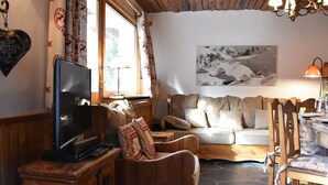 Ein gemütliches Wohnzimmer mit einer Couch, Holzstühlen, einem Fernseher und einem Steinfußboden.
