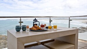 A breakfast table with croissants, eggs, jam, and orange juice on a balcony overlooking the sea. - The Penthouse Bay View (Westward Ho!)
