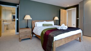 A bedroom with a bed, bedside tables, lamps, and a bathroom visible through an open door. - The Penthouse Bay View (Westward Ho!)