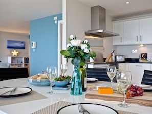 A dining table set with plates, glasses, a vase with flowers, and a cheese block. - The Penthouse Bay View (Westward Ho!)