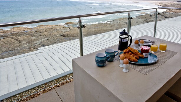 A balcony with a table set for breakfast overlooking a beach. - The Penthouse Bay View (Westward Ho!)