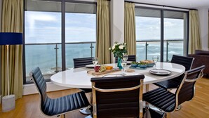 A dining area with a round table, four chairs, and a view of the ocean through large windows. - The Penthouse Bay View (Westward Ho!)