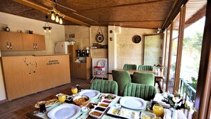 A dining area with a table set for breakfast, a kitchen in the background, and a view of the outdoors. - Orion Cave Hotel (Ürgüp)