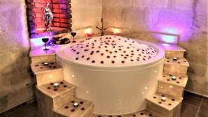 A circular hot tub with rose petals scattered on the surface, surrounded by steps with candles. - Orion Cave Hotel (Ürgüp)