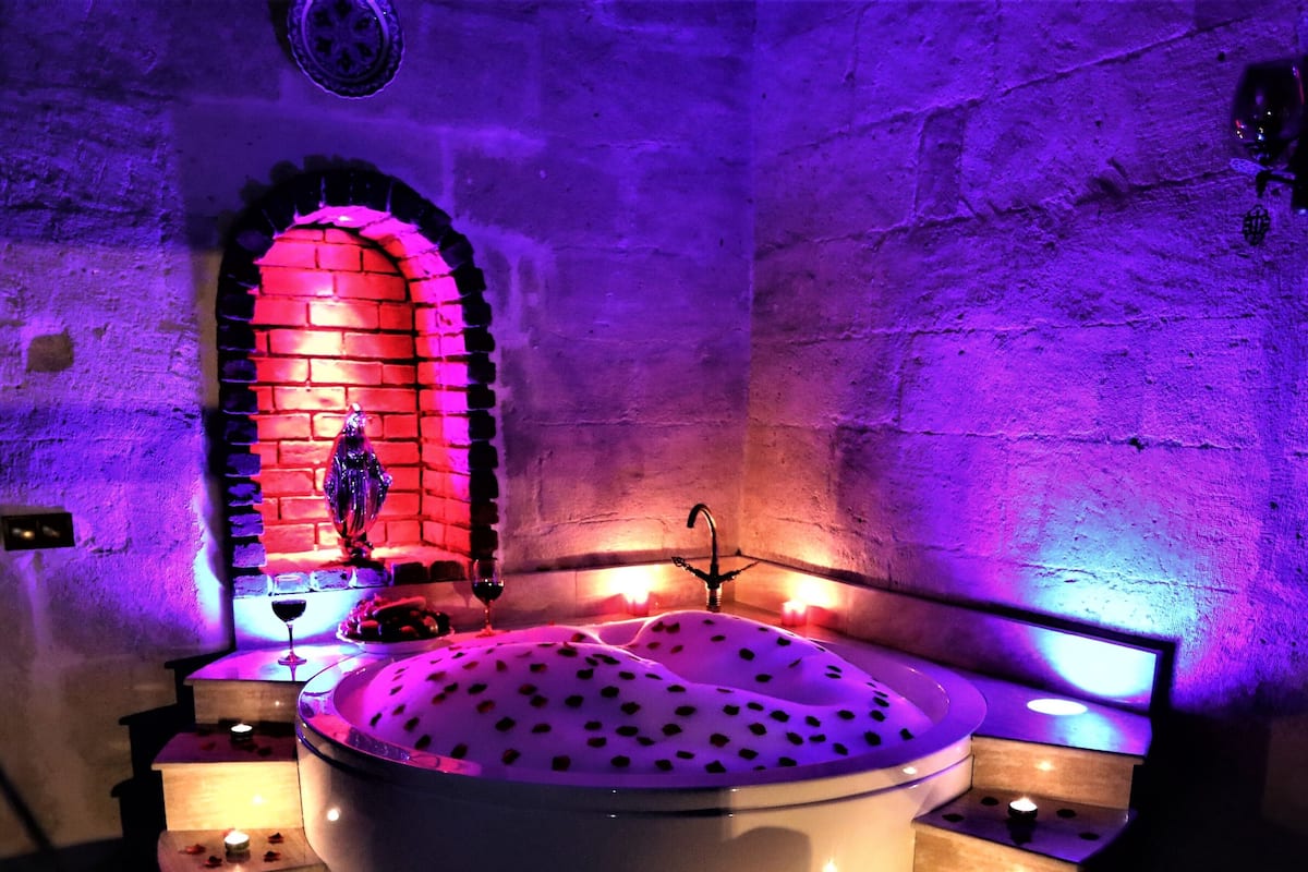 A bathtub with rose petals and candles, surrounded by steps and a brick wall.