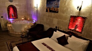 A room with a large bed, a small seating area, a bathtub, and a wall with a red brick design. - Orion Cave Hotel (Ürgüp)