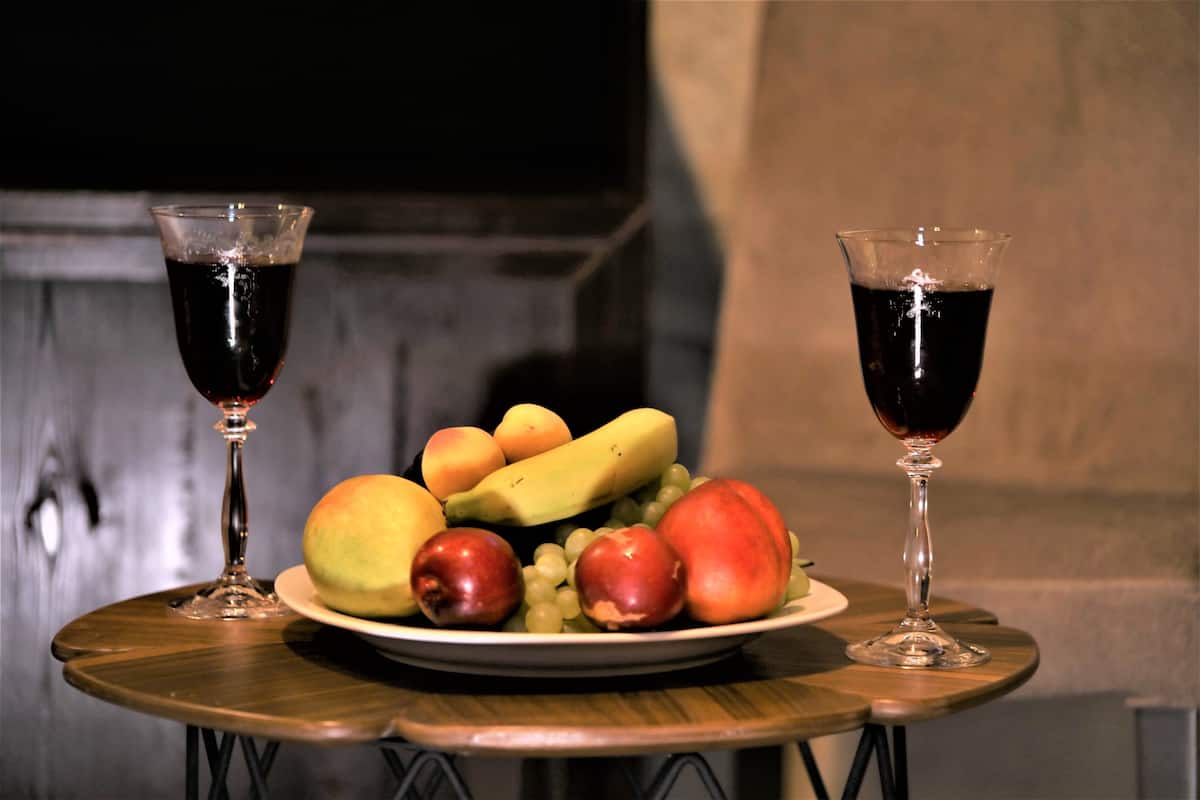 A table with a plate of fruit and two glasses of red wine.