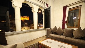 A living room with a sofa, a coffee table, and a view of a cityscape at night. - Orion Cave Hotel (Ürgüp)