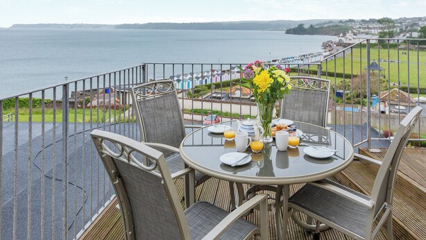 A balcony with a table set for breakfast, overlooking a body of water and a coastal area. - Ideally positioned apartment with large balcony overlooking Goodrington Beach. (Paignton)