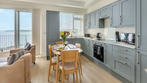 A modern kitchen with grey cabinets, a dining area with a table and chairs, and a view of the sea through large windows. - Ideally positioned apartment with large balcony overlooking Goodrington Beach. (Paignton)
