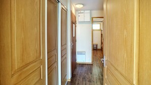 Un couloir étroit, avec des portes en bois de chaque côté, un plafond blanc et une petite fenêtre au fond.