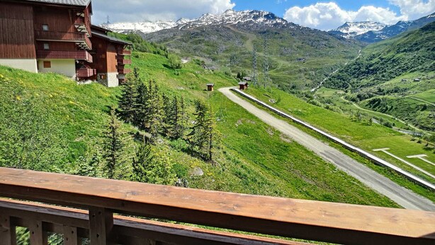 Un chalet en bois doté de balcons, une route menant à une montagne et un ciel dégagé.