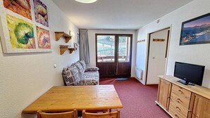 Una habitació acollidora amb taula i cadires de fusta, un sofà, una televisió i obra d'art a les parets.