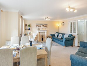 A living room with a sofa, chairs, a dining table set, a fireplace, and a clock on the wall.