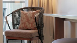 A wicker chair with a cushion, a small table, and a lamp in a room with a view of a building outside. - BEST RATE!  ADA Studio Ala Moana Condominium (AH01) (Honolulu)