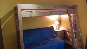 Ein Stockbett mit Holzbettrahmen, einer blauen Matratze, einem Nachttisch mit Lampe und einer Stehleiter.