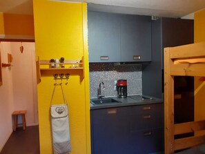Compact kitchen area with sink, coffee maker, and shelf, offering a convenient space for preparing meals.