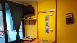 Ein Zimmer mit Holztisch und Stühlen, einem an der Wand montierten Fernseher und einem fenster mit Vorhängen.