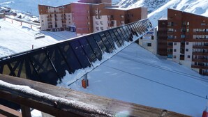 Eine Seilbahn mit Metallkonstruktion und Holellbohrungen, umgeben von schneebedeckten Bergen und Gebäuden mit mehreren Etagen und Balkonen.