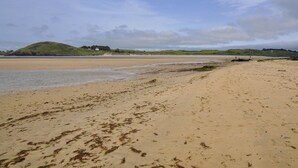 A beach with a sandy shore, a small hill in the background, and a body of water. - 4 bedroom accommodation in Padstow (Padstow)