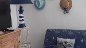A room with a wooden cabinet, a television, a blue patterned sofa, a small table, and a wall with several hats.