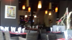A restaurant with round tables and wicker chairs, overhead lighting, and a tiled floor.