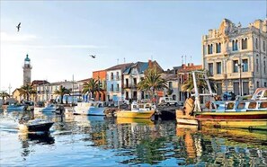 A harbor with boats docked, buildings with classical architecture, and a lighthouse in the background.